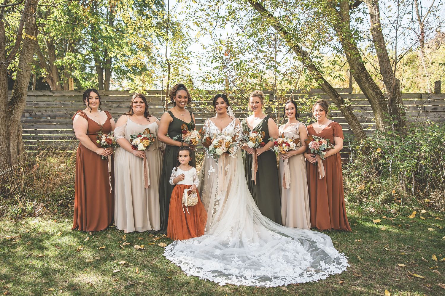 Wedding party in earth tones poses together in outdoor autumn setting.
