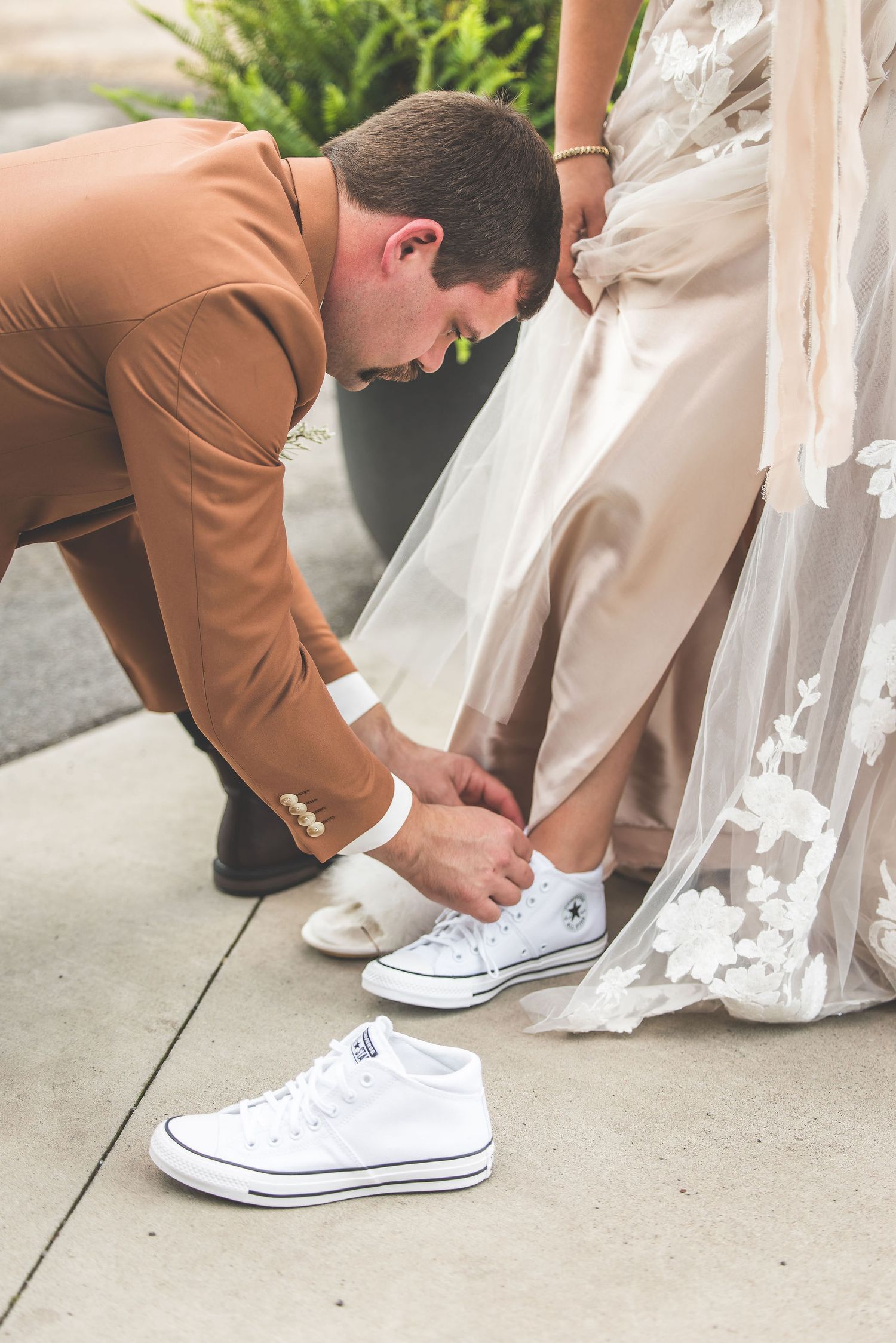 Close-up of white Converse sneakers being put on under wedding dress.