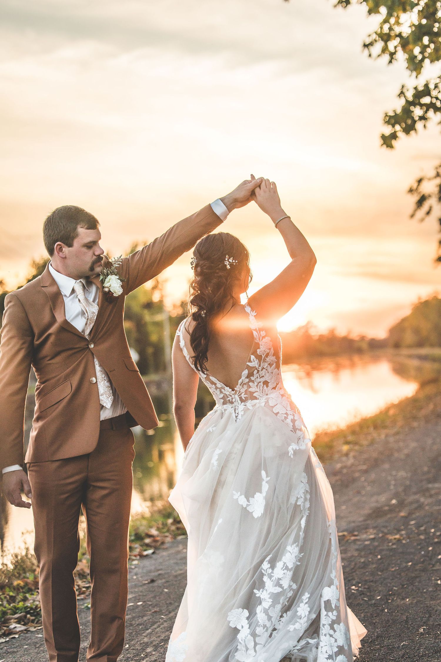 Dancing wedding couple silhouetted against sunset sky by the water.