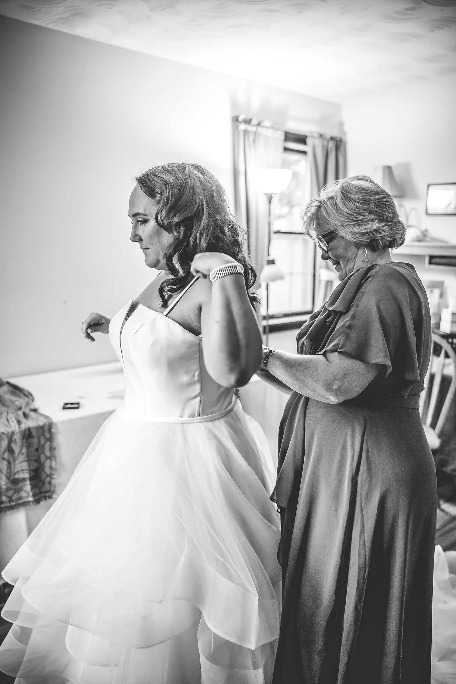 A series of black and white photos showing the process of putting on a wedding dress.