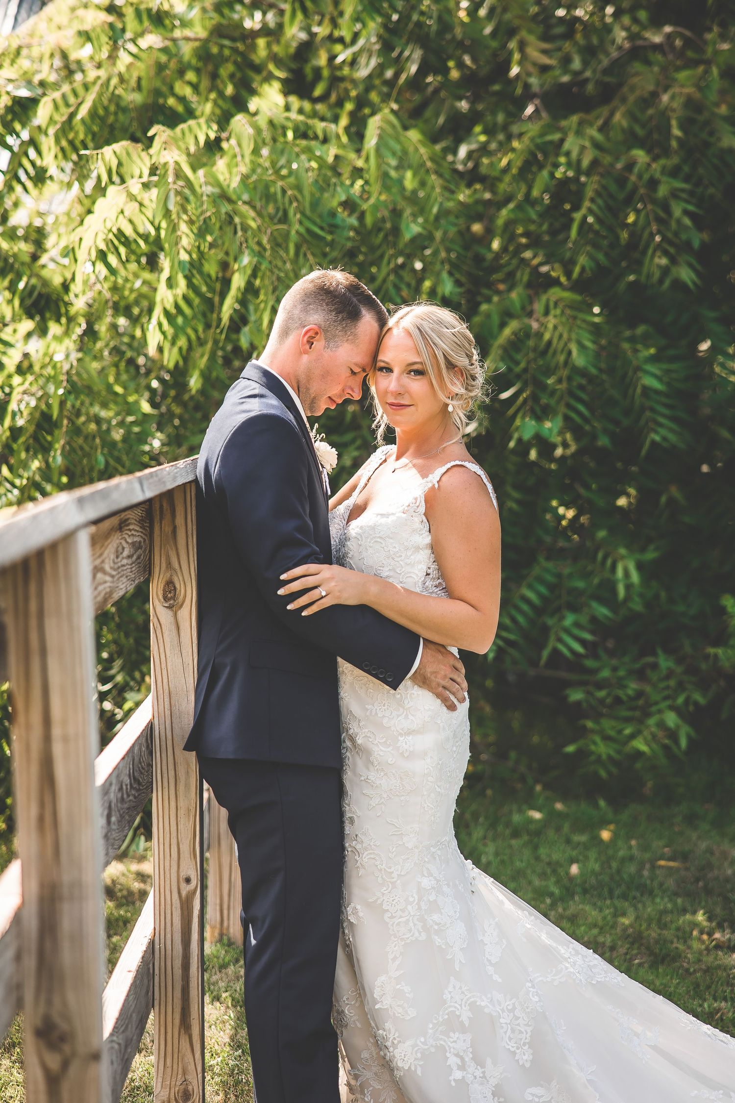 An intimate wedding portrait of a couple sharing a tender moment on a wooden bridge in nature.