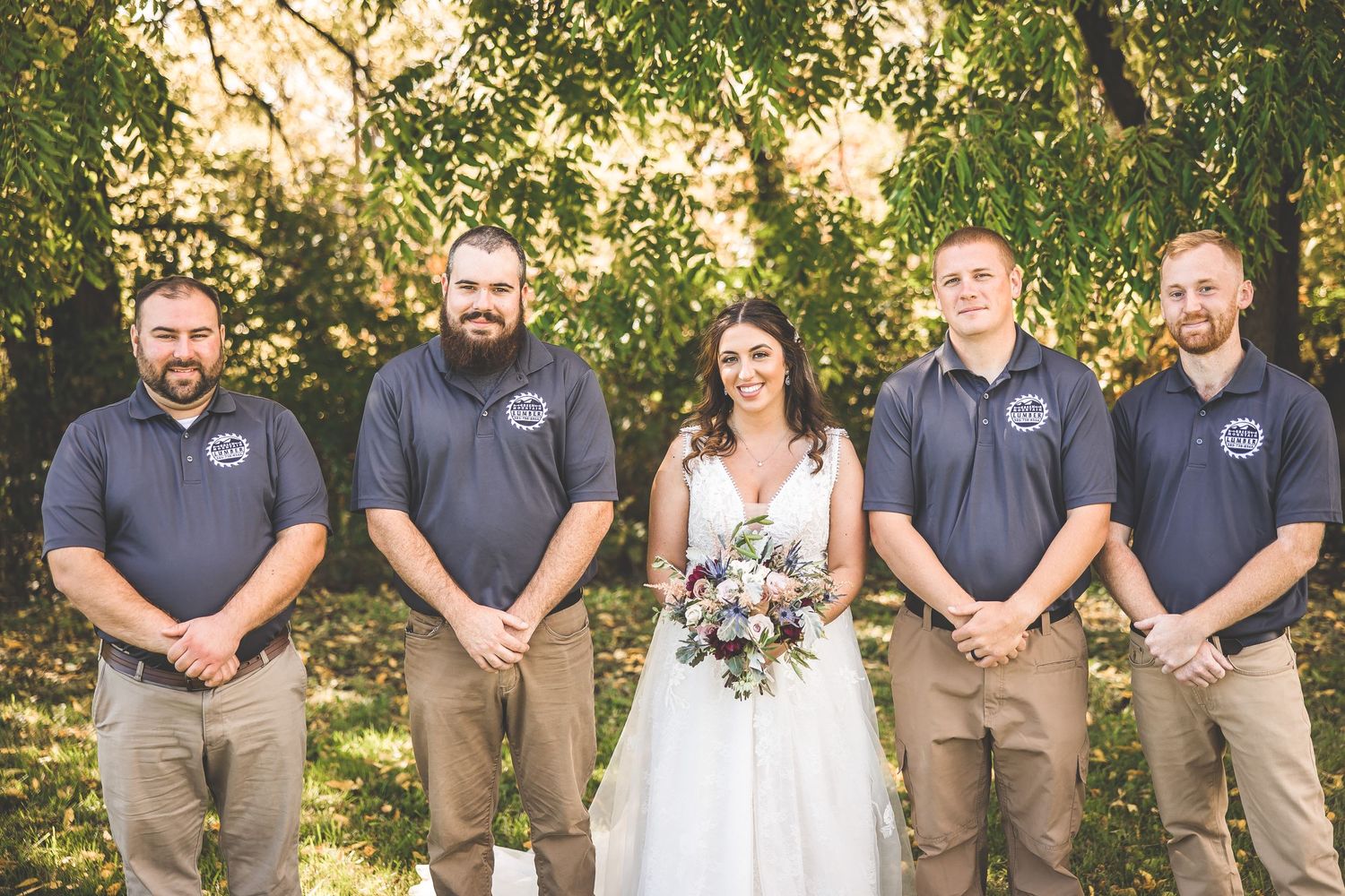 Wedding party in matching gray polos and khakis poses with bride in white dress.
