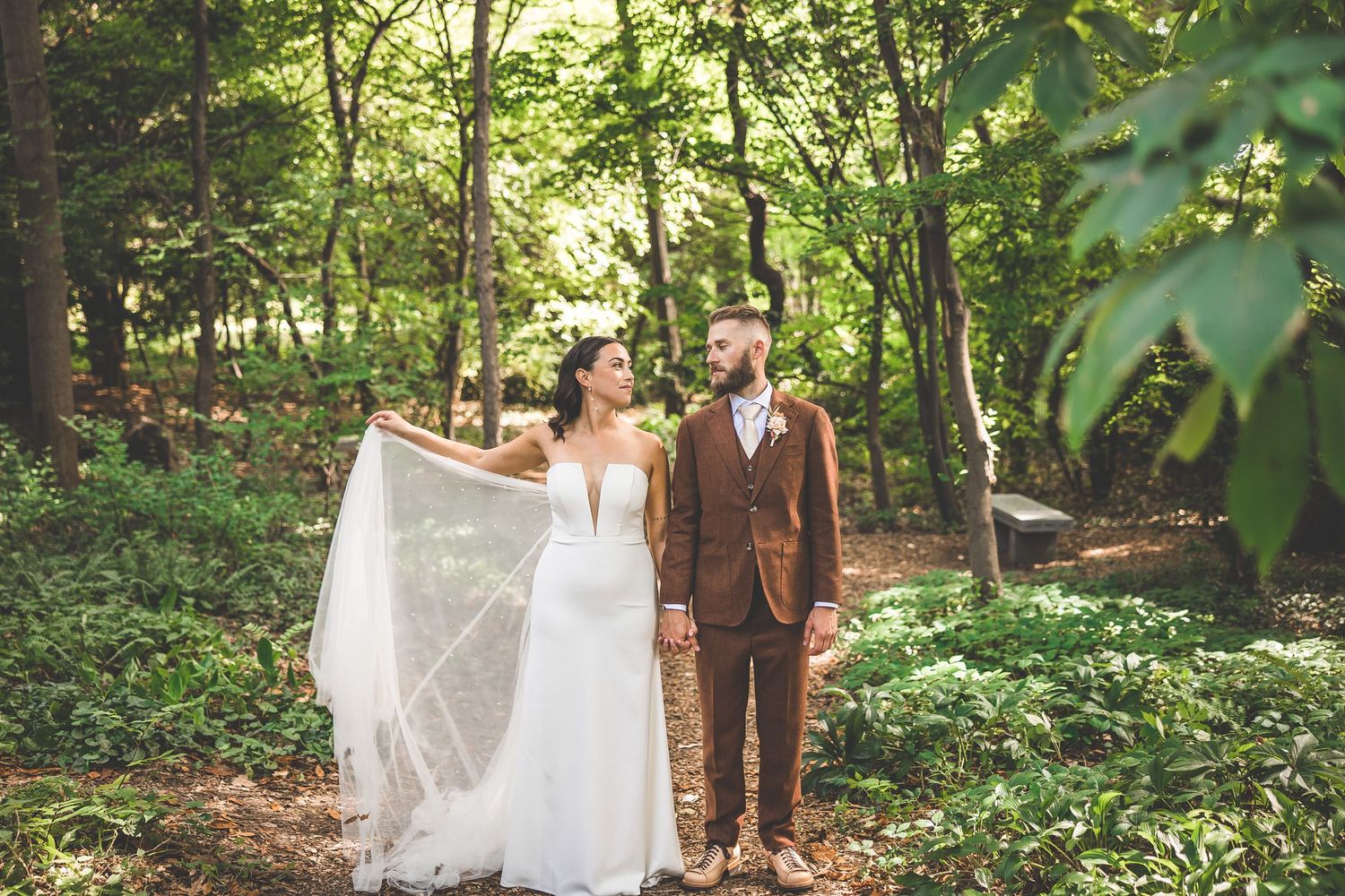 Newlyweds walk hand in hand along a serene woodland trail during their forest wedding.