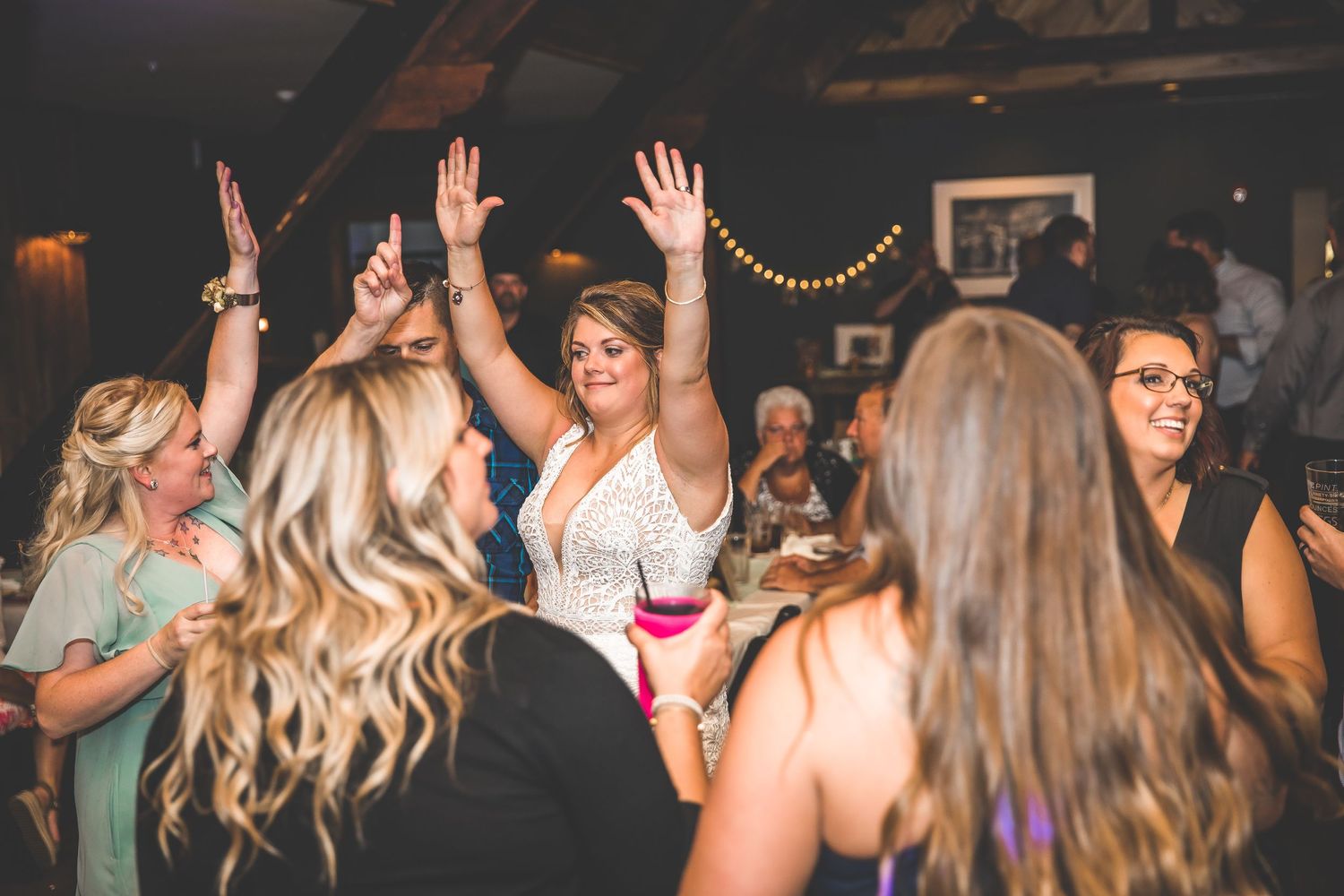 Wedding party dancing with raised hands on the dance floor during evening celebration.