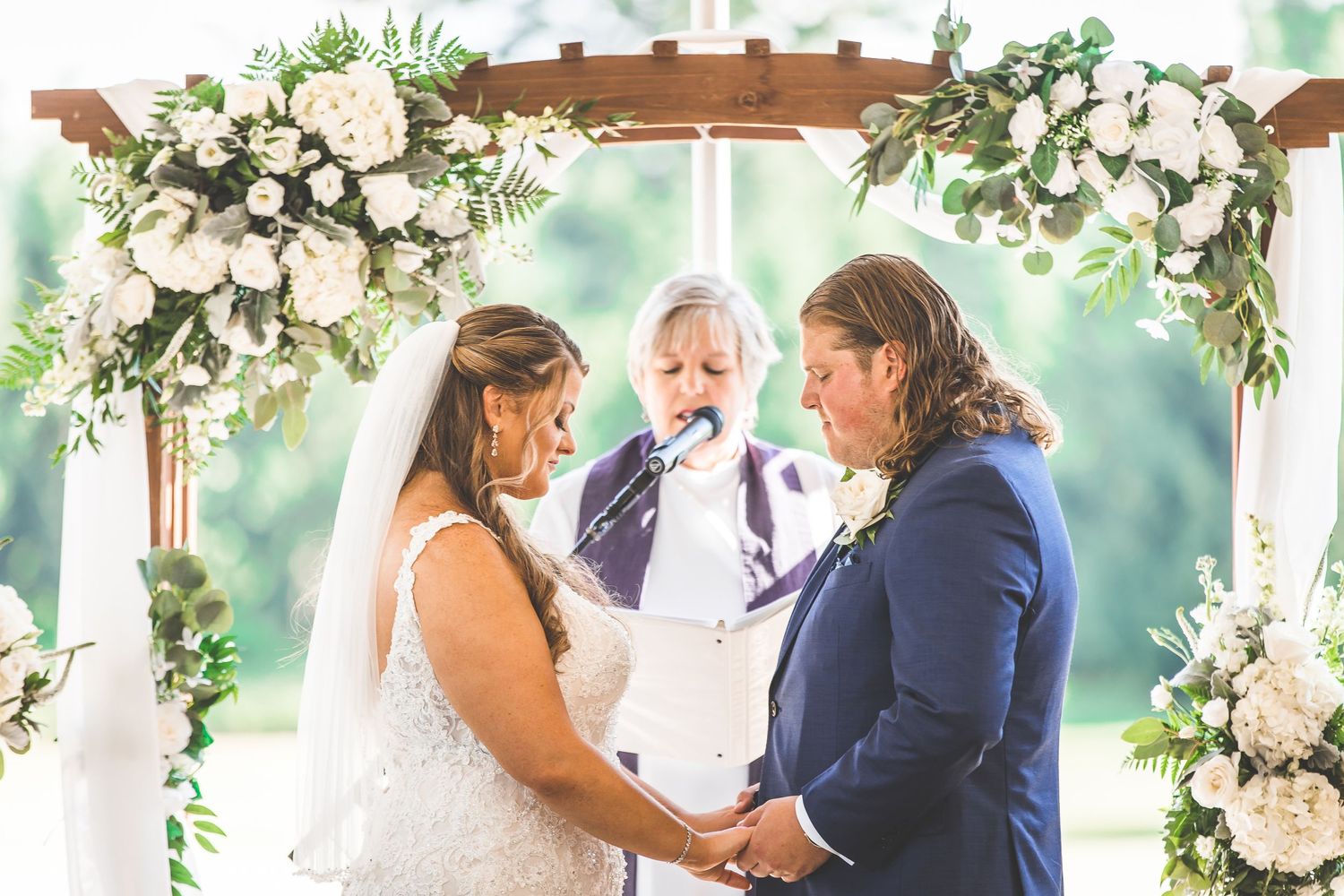Wedding ceremony arch decorated with white floral arrangements under outdoor tent.