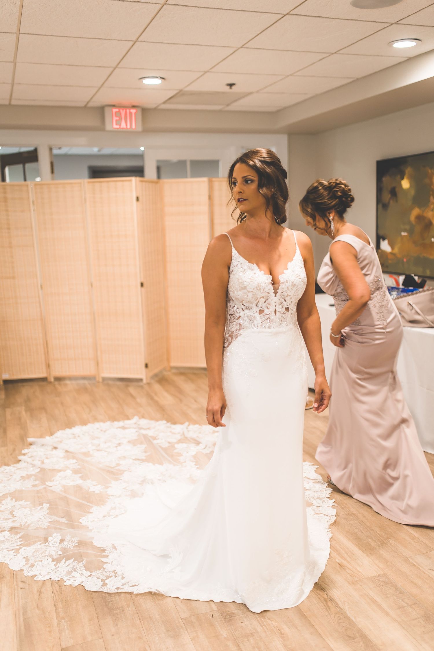 Wedding dress with lace details trailing on wooden floor during preparation.