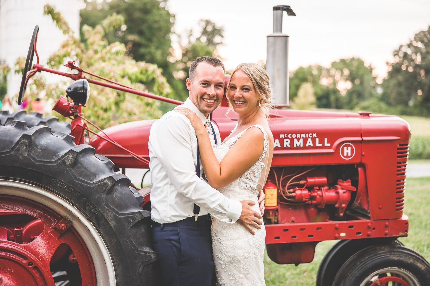 A happy couple poses in front of a vintage red Farmall tractor on their wedding day.