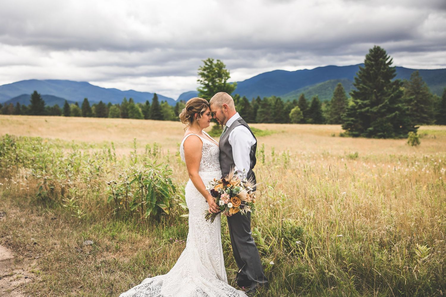 A wedding photoshoot in a scenic mountain meadow with dramatic cloudy skies.