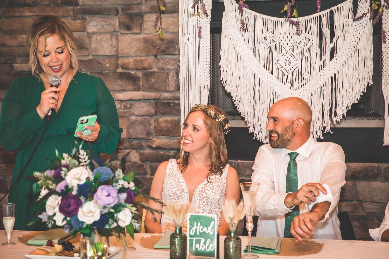 Wedding reception head table decorated with macrame backdrop and floral arrangements.