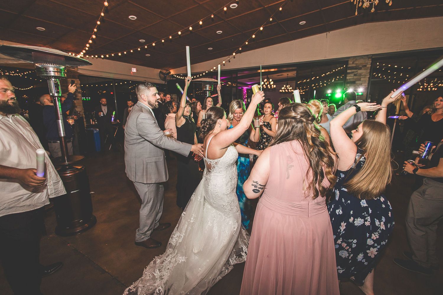 Wedding party dancing and celebrating on the dance floor under twinkling lights.