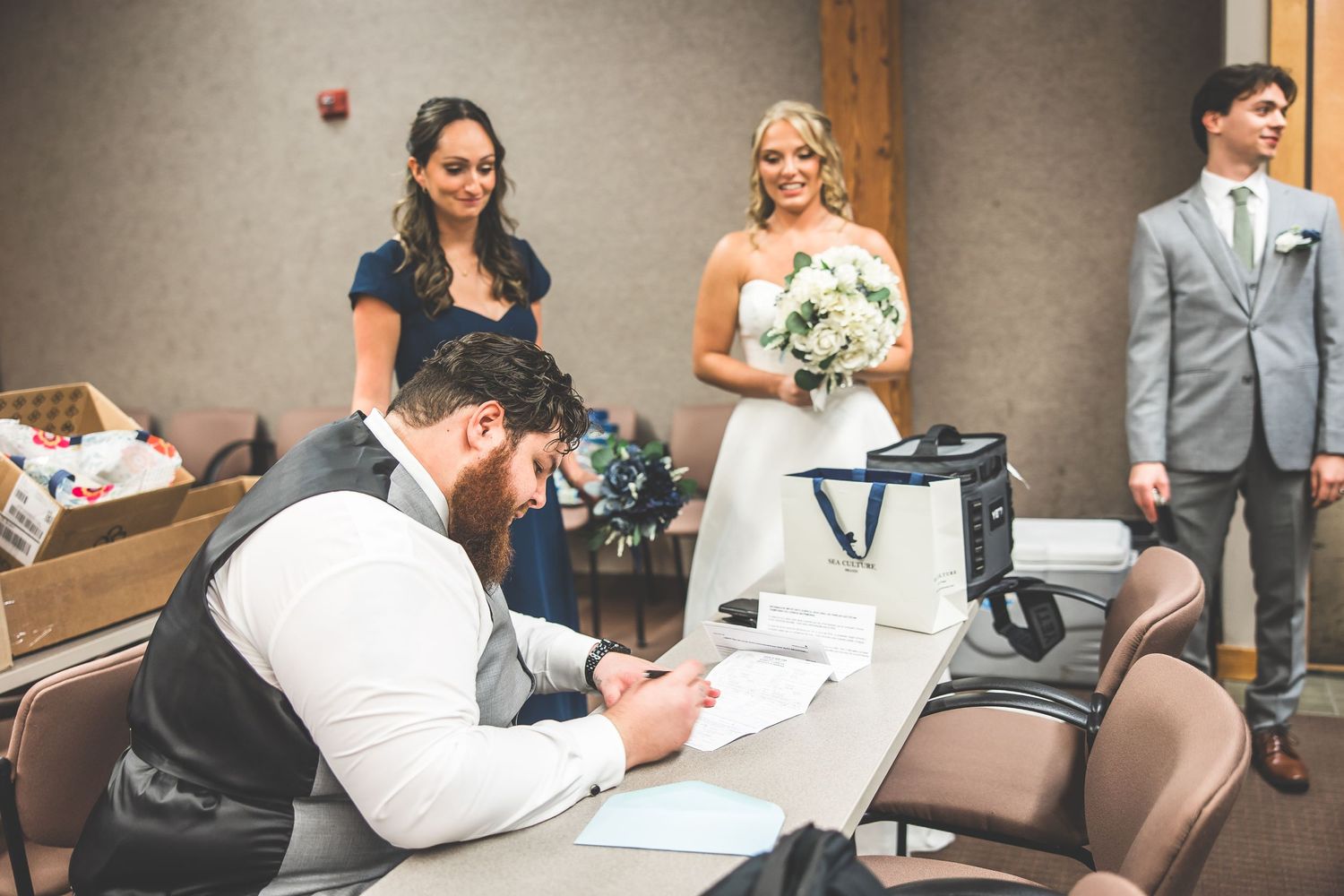 Wedding party signing documents at a registration table with papers and pens.