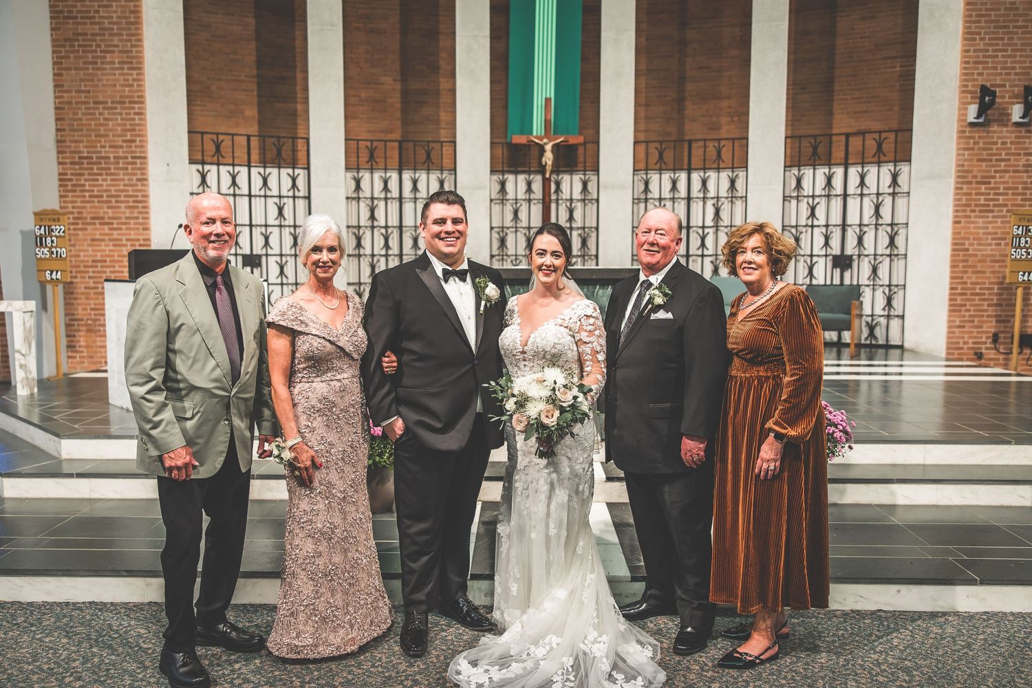 Wedding party gathered outside brick church with green columns and decorative ironwork.