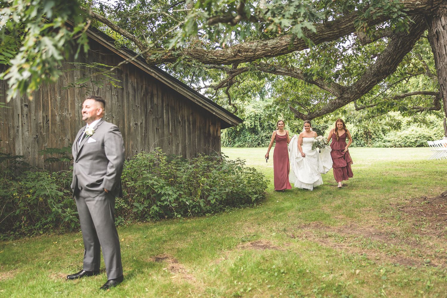 Rustic wedding photo shoot in front of weathered barn with bridesmaids in burgundy dresses.