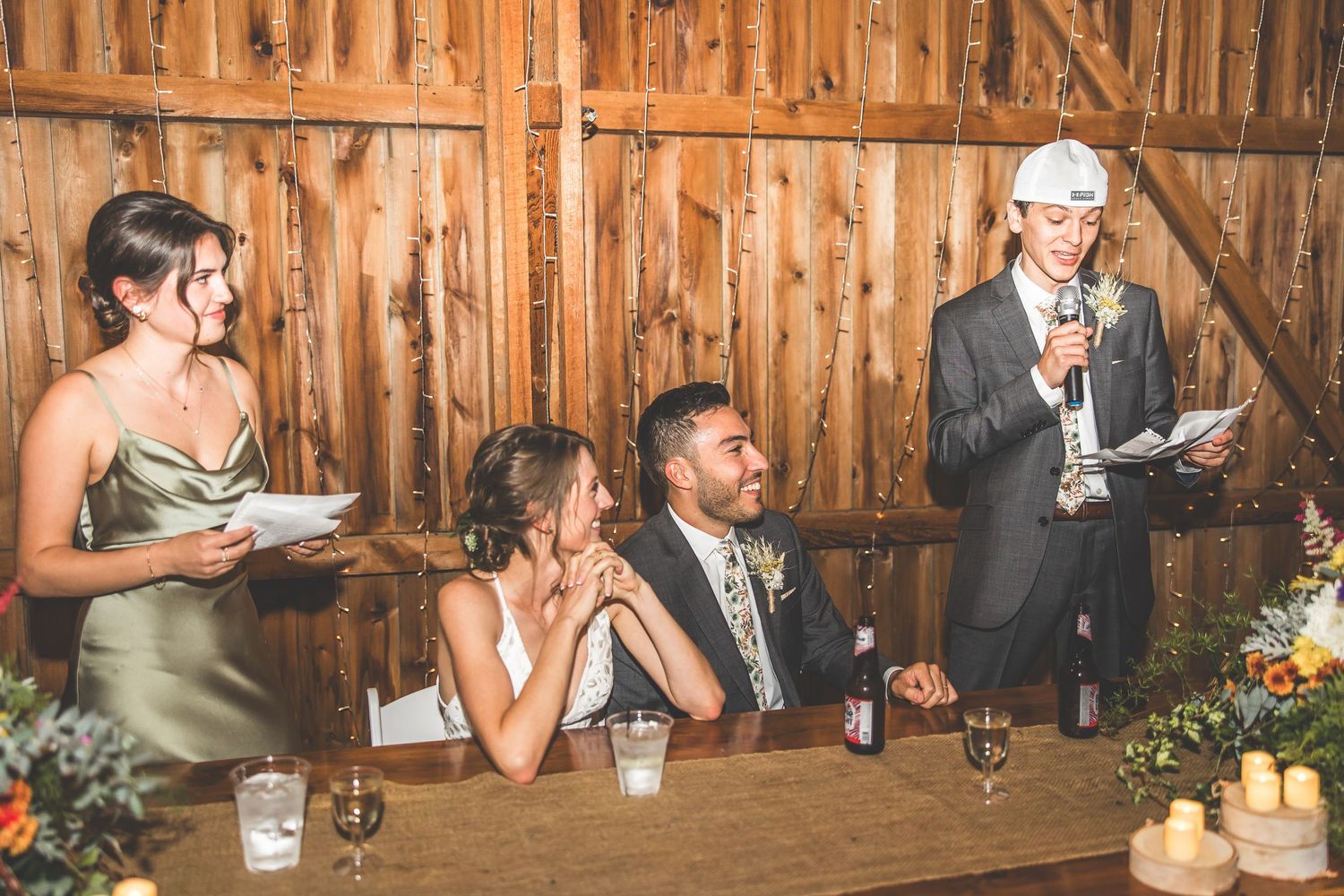 Wedding guests celebrate at long tables inside a rustic barn reception venue.