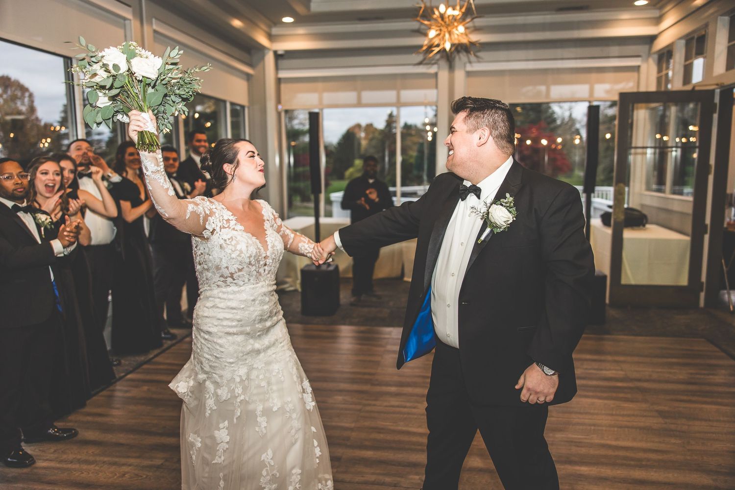 Couple performs first dance in elegant reception hall with wooden floors and decorative ceiling.