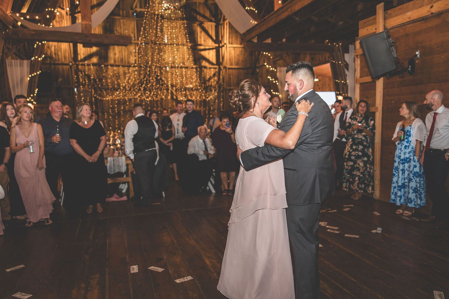 Couple sharing intimate dance moment in rustic barn venue with string lights and wooden beams.