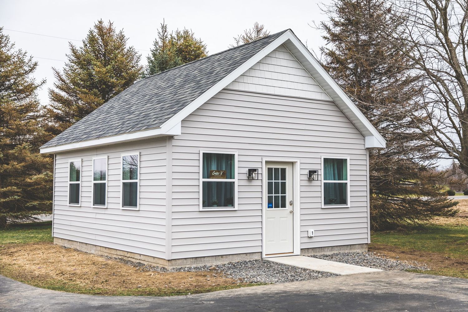 White vinyl siding on a ranch-style house exterior with evergreen trees in the background.