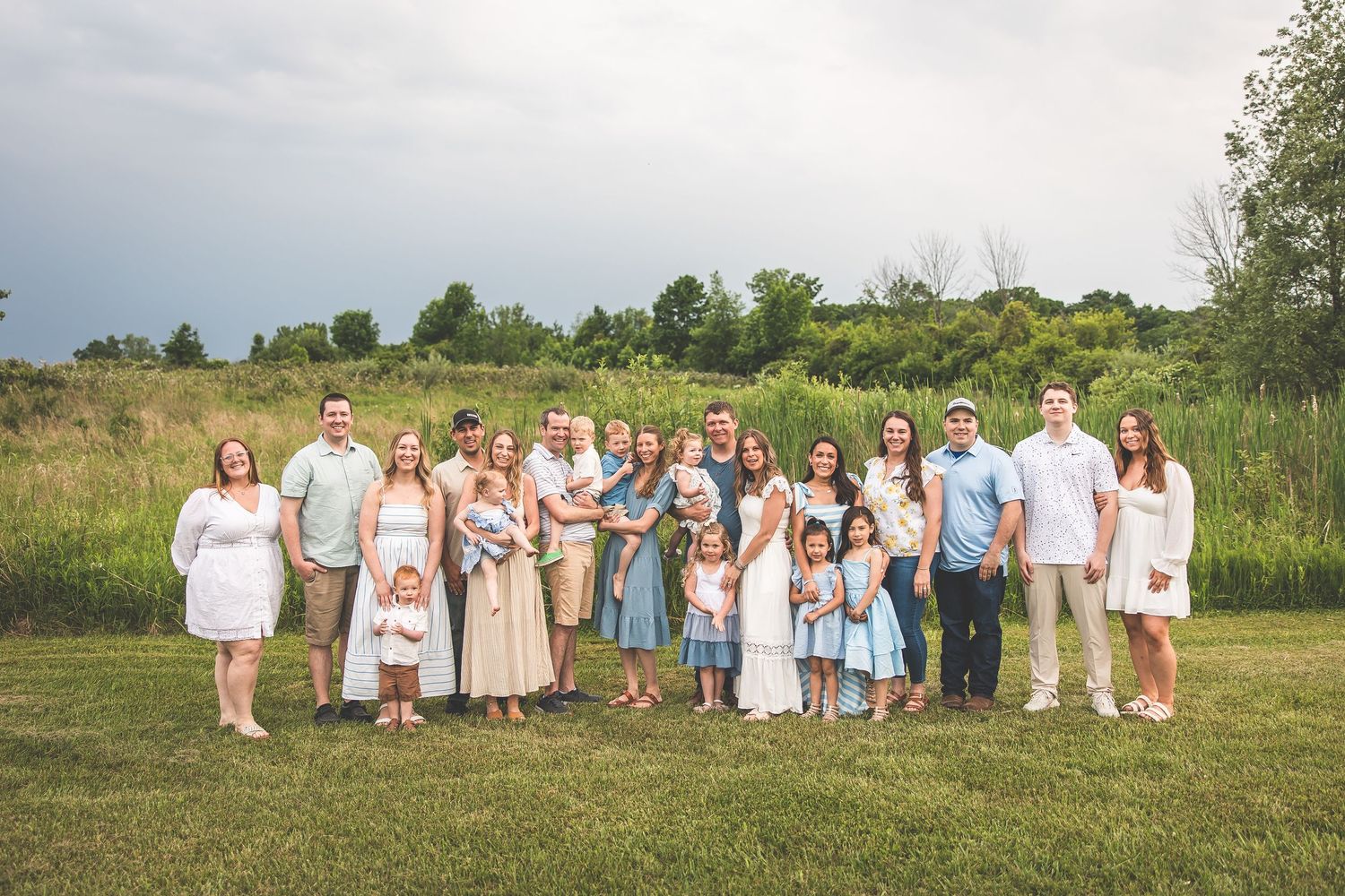 Large family group in coordinated pastel outfits posing together in outdoor field setting.