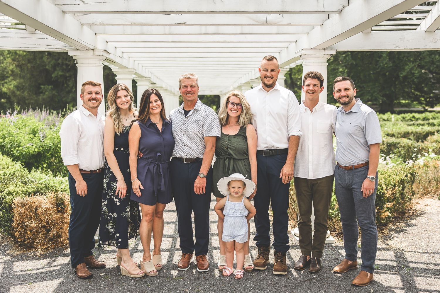 A multi-generational family poses together under a white pergola in a garden setting.