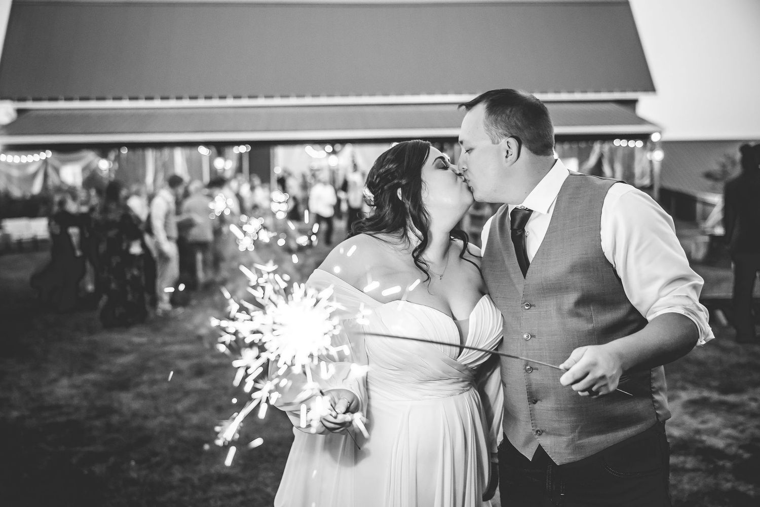 Wedding guests dancing and celebrating at an outdoor reception with sparklers and festive lighting.