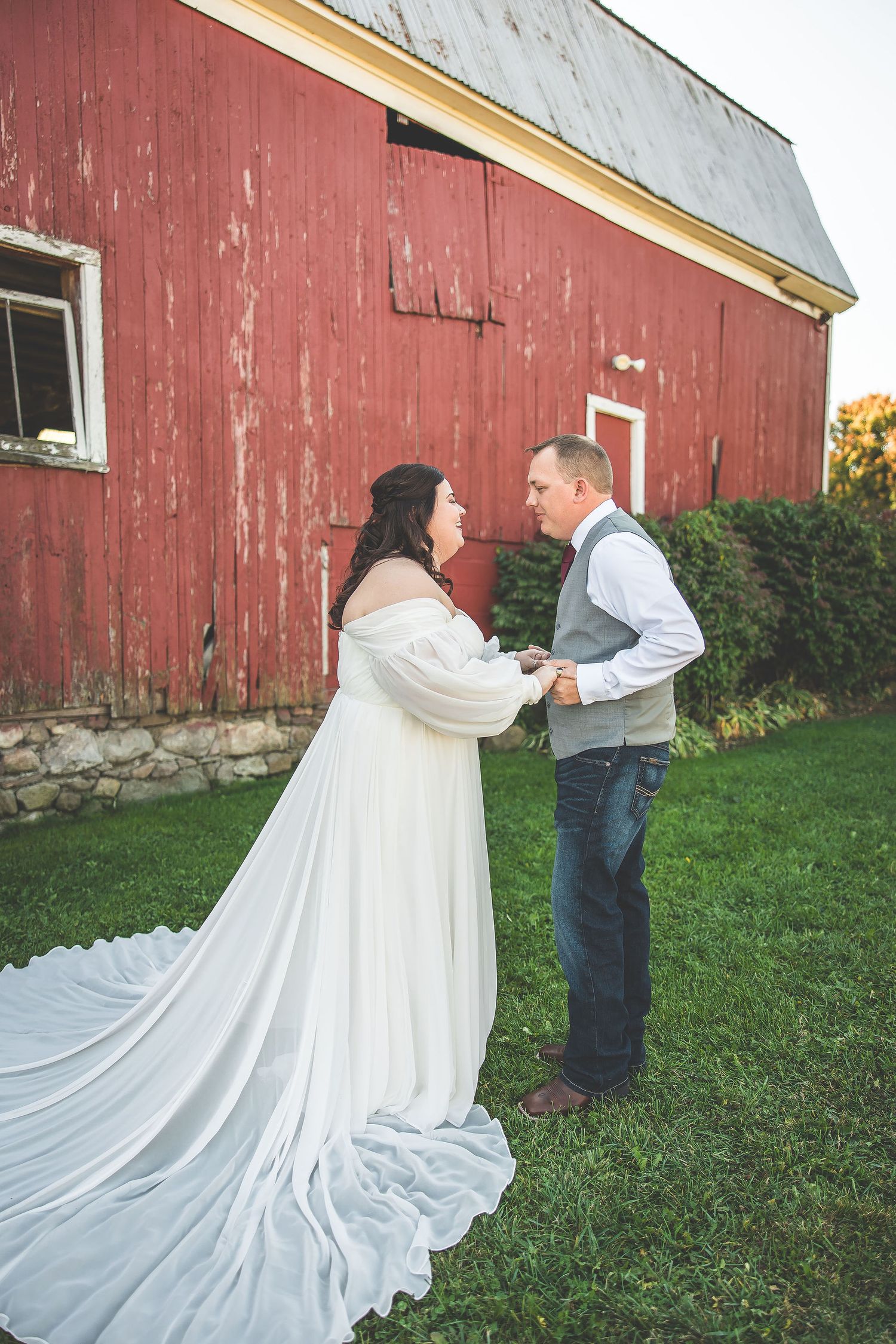 A couple poses for romantic wedding photos against a rustic red barn backdrop.