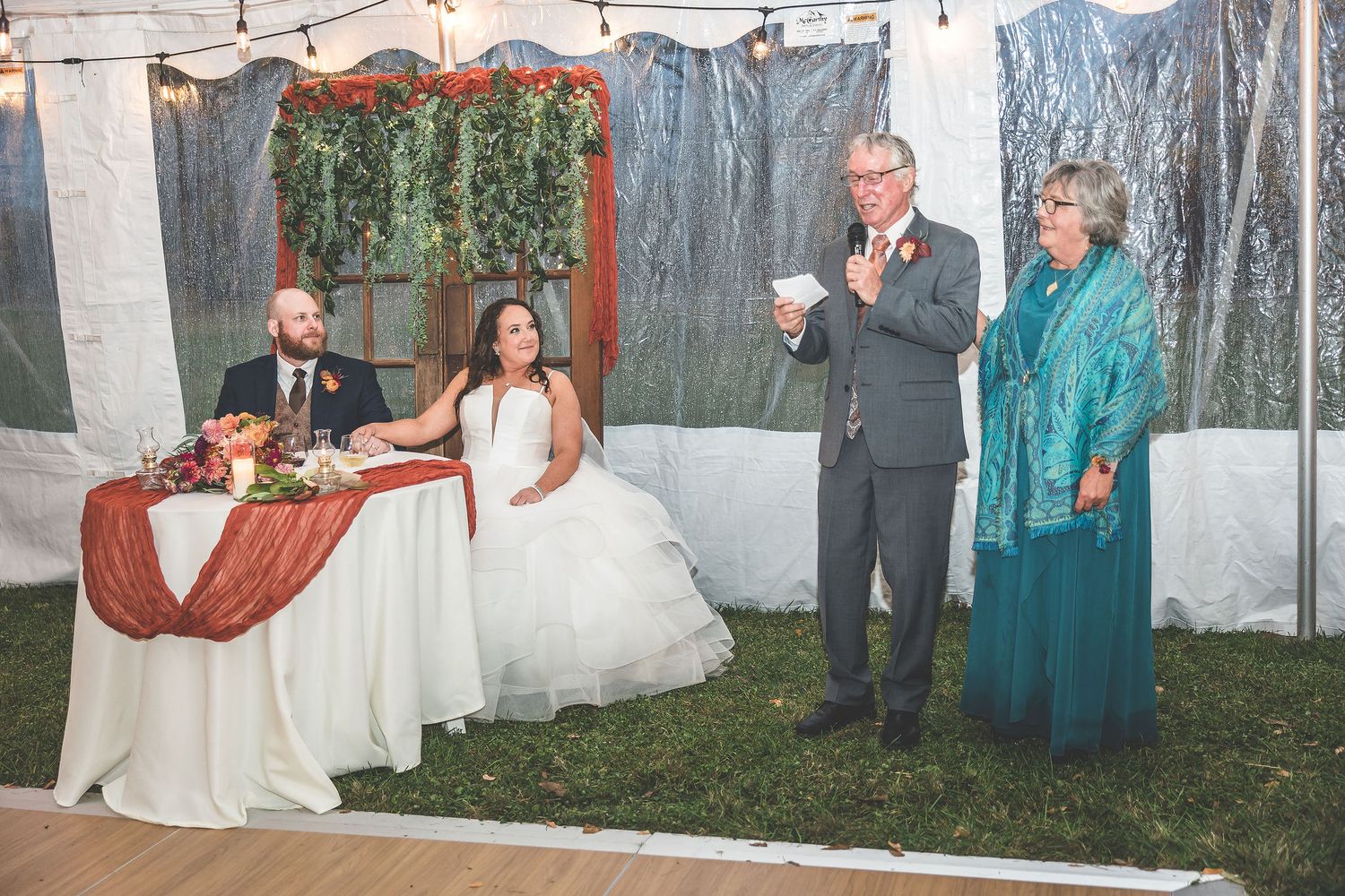 Outdoor wedding tent decorated with string lights and white fabric panels.