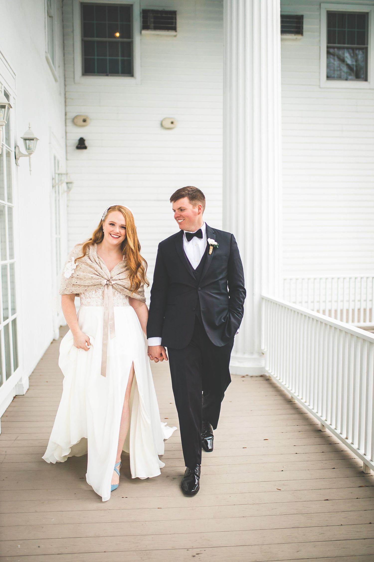 Playful wedding couple walking and laughing together on a white columned porch.