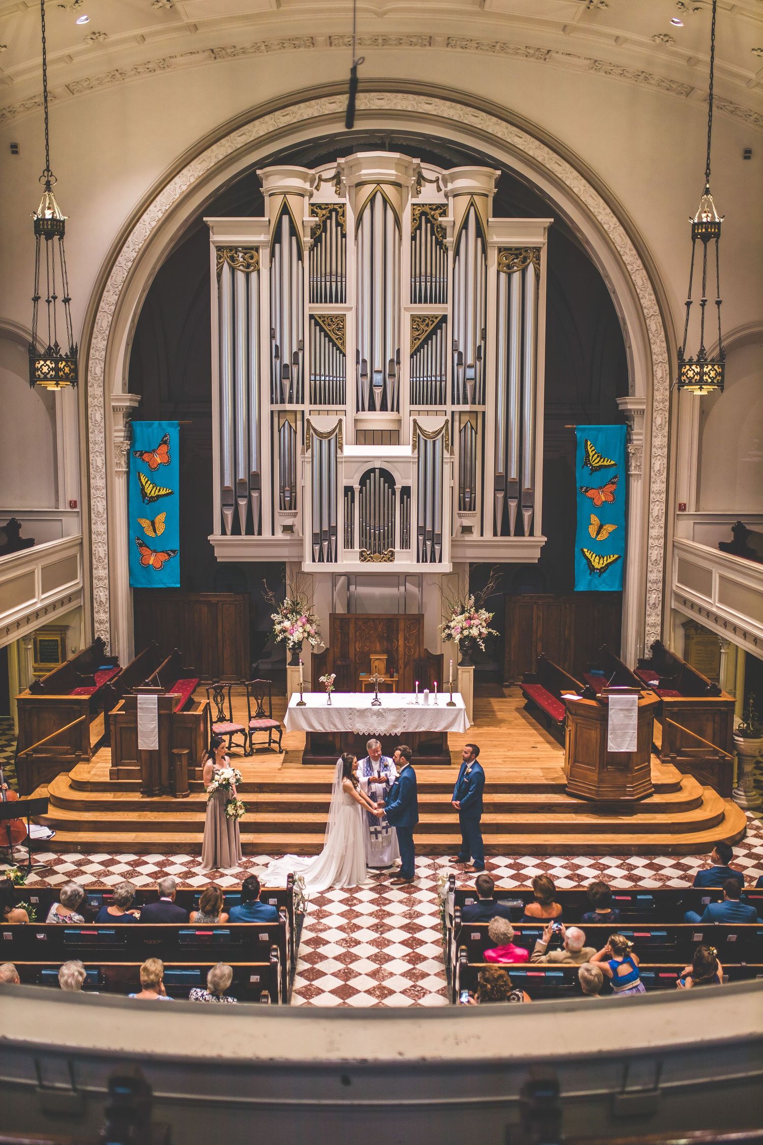 Wedding ceremony in a historic church with grand pipe organ and checkerboard floor.