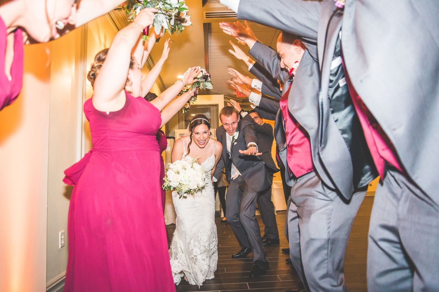 Wedding reception dance floor filled with guests celebrating in pink and orange lighting.