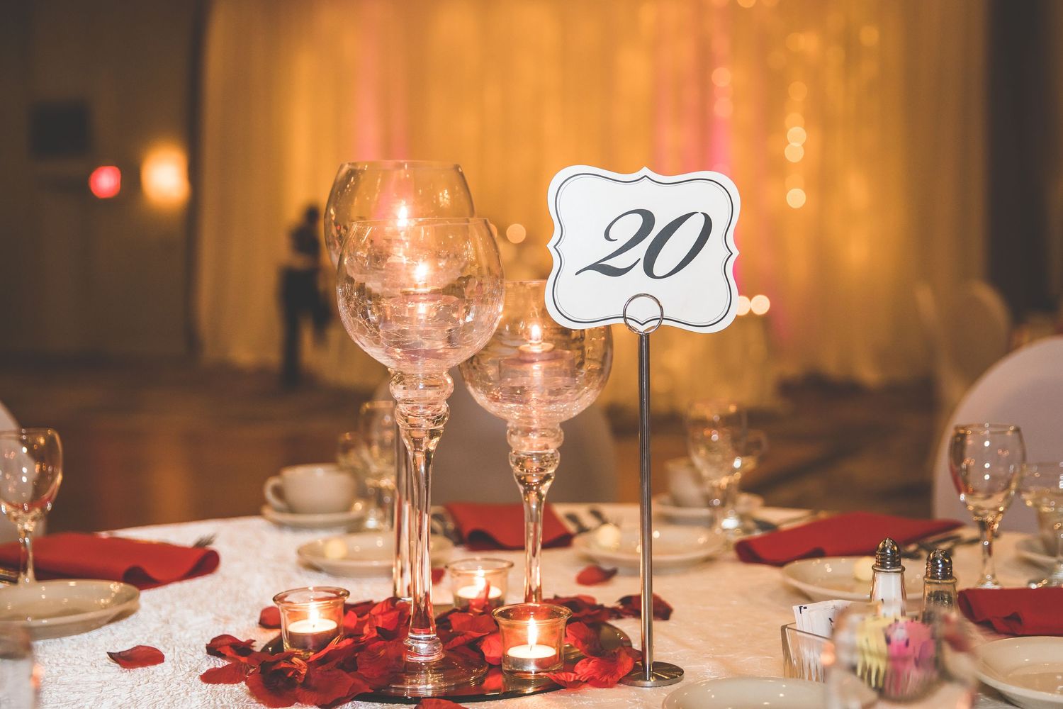 Wedding reception table settings with red rose petals and table number decorations.