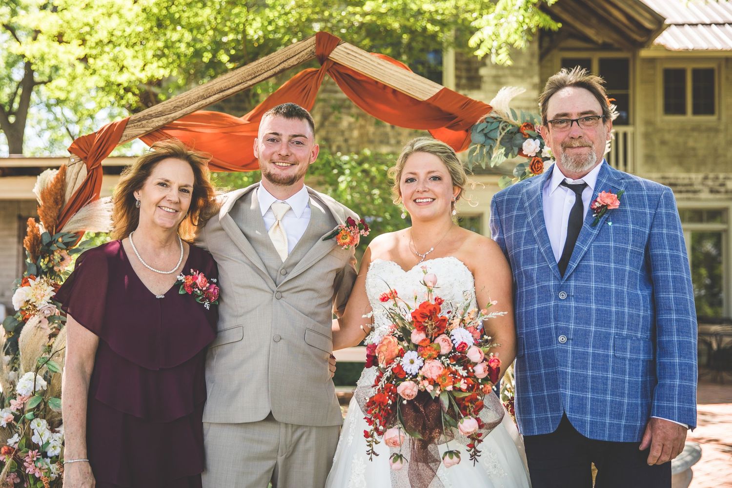 Small wedding group poses under orange draped arch with floral decorations.