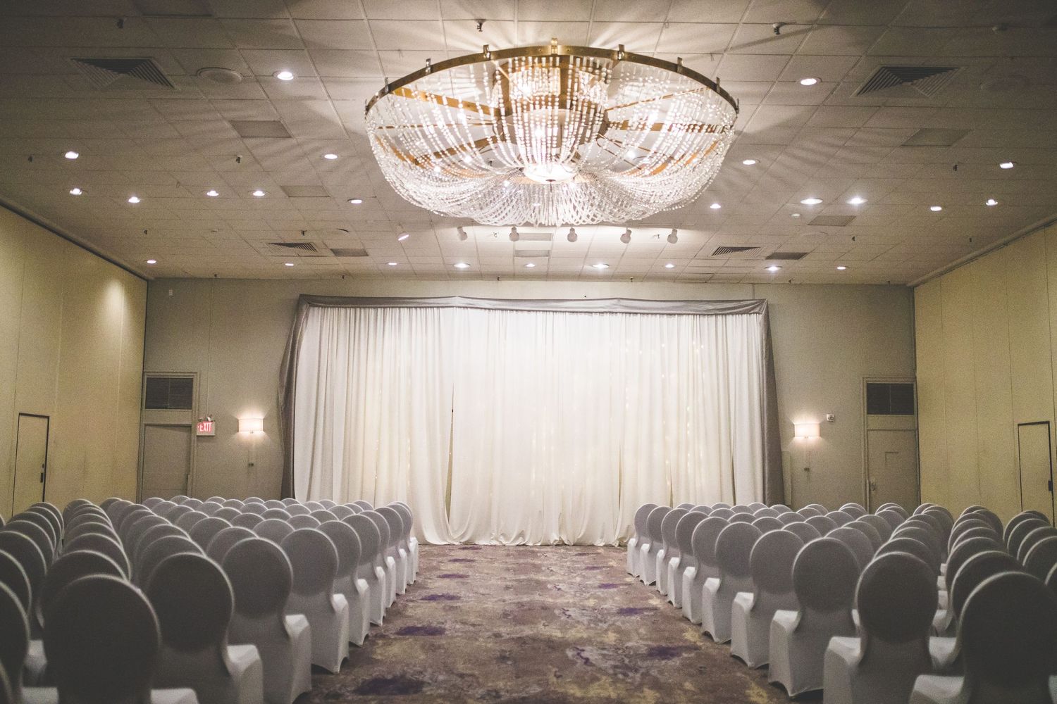 Panoramic view of an elegant wedding ceremony space with white chairs and crystal chandelier.