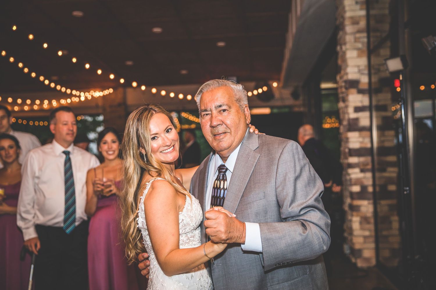 Wedding guests dancing together under romantic string lights at an indoor venue.