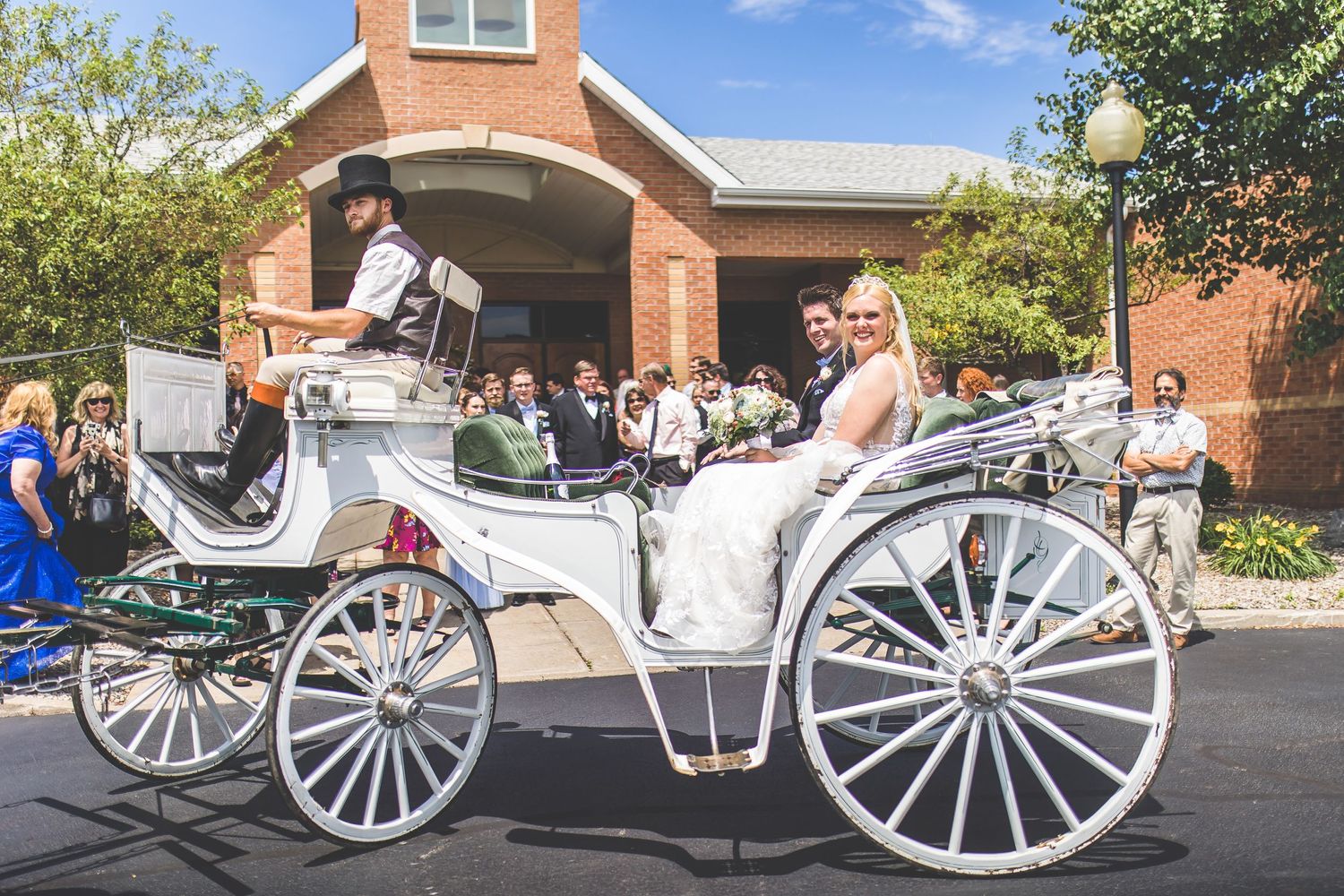 Classic white horse-drawn carriage parked outside brick church building.