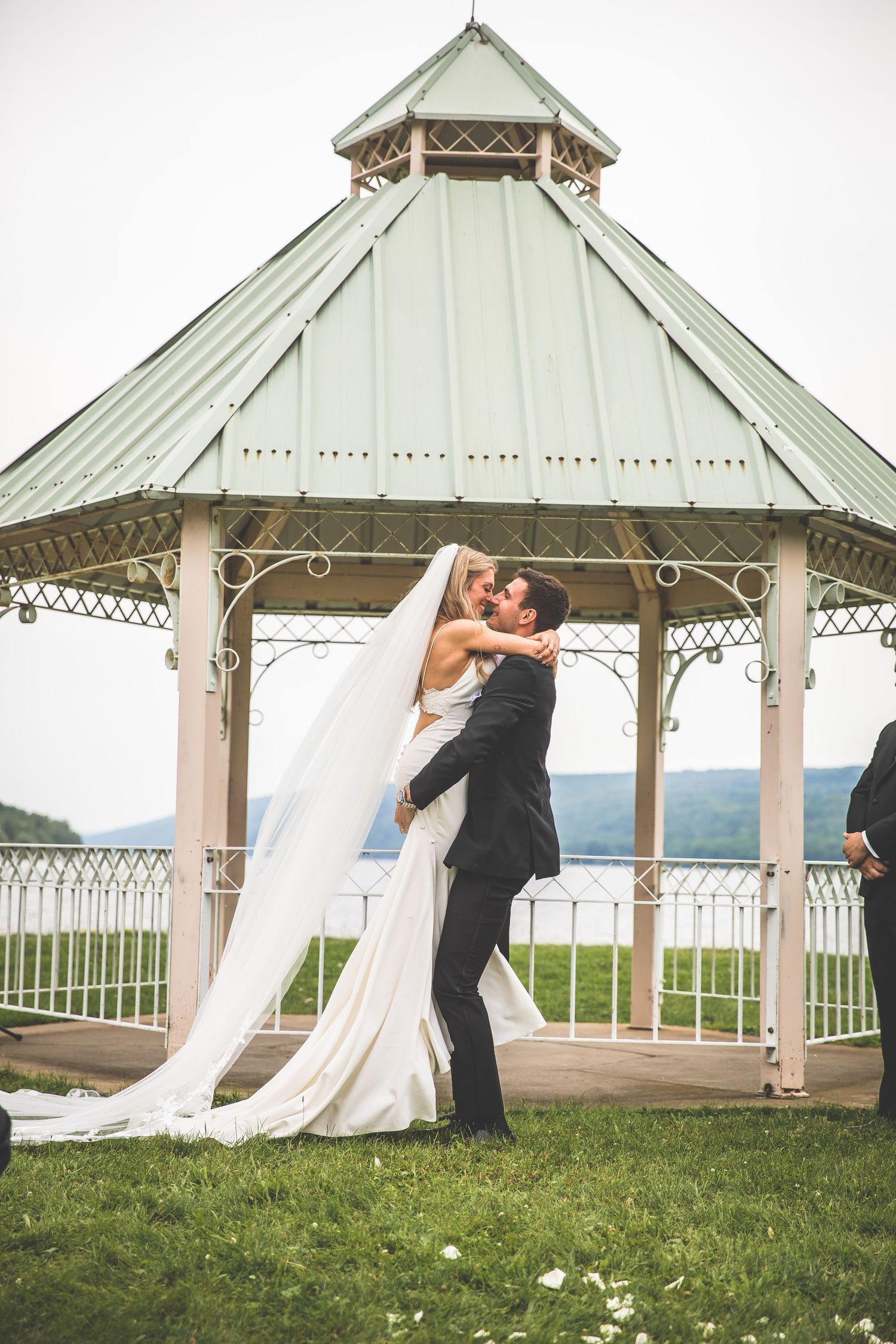 Couple sharing first kiss as newlyweds under white gazebo at outdoor wedding venue.