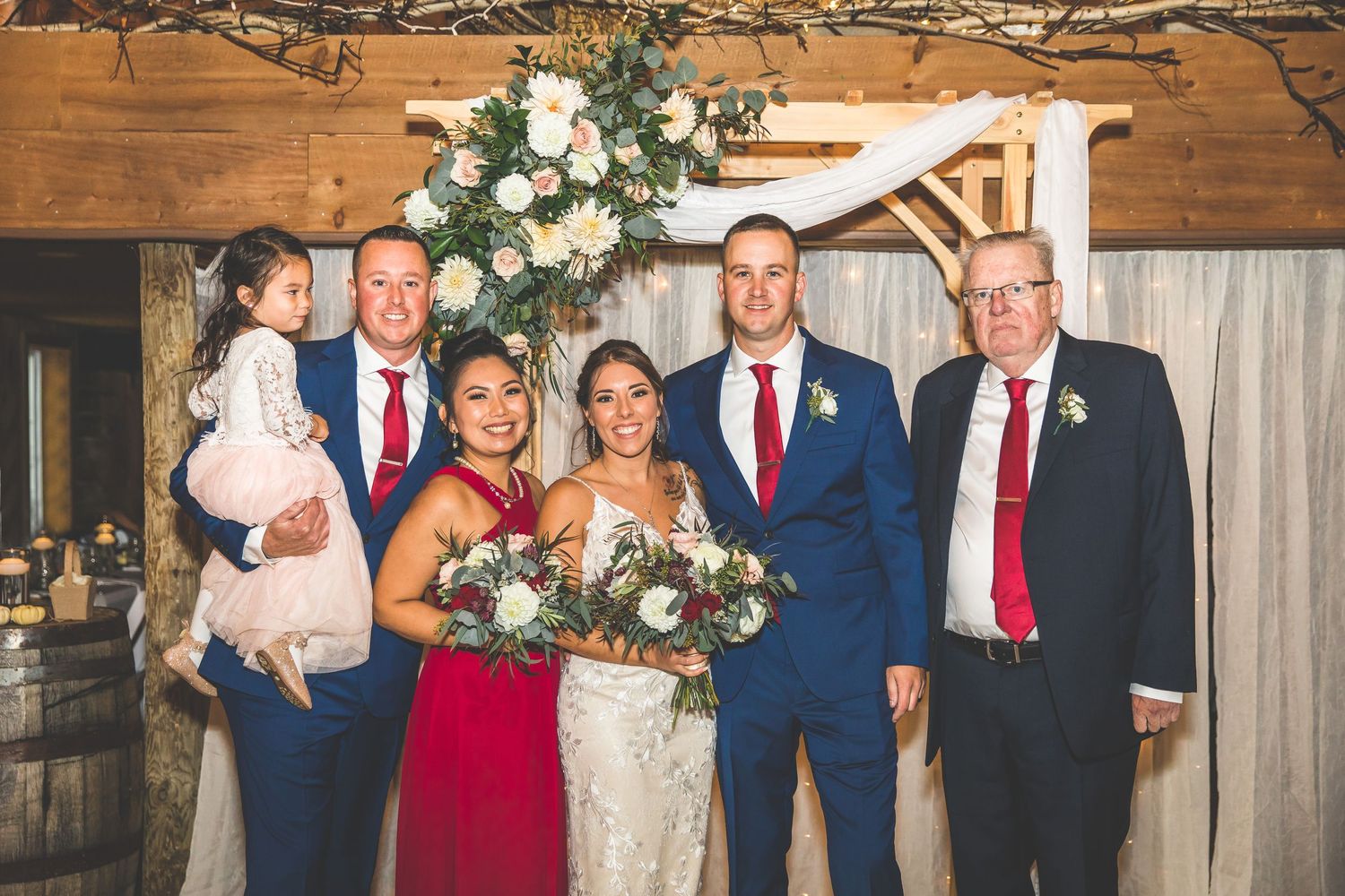 Wedding party members in coordinated navy and red attire gathered for formal photos.