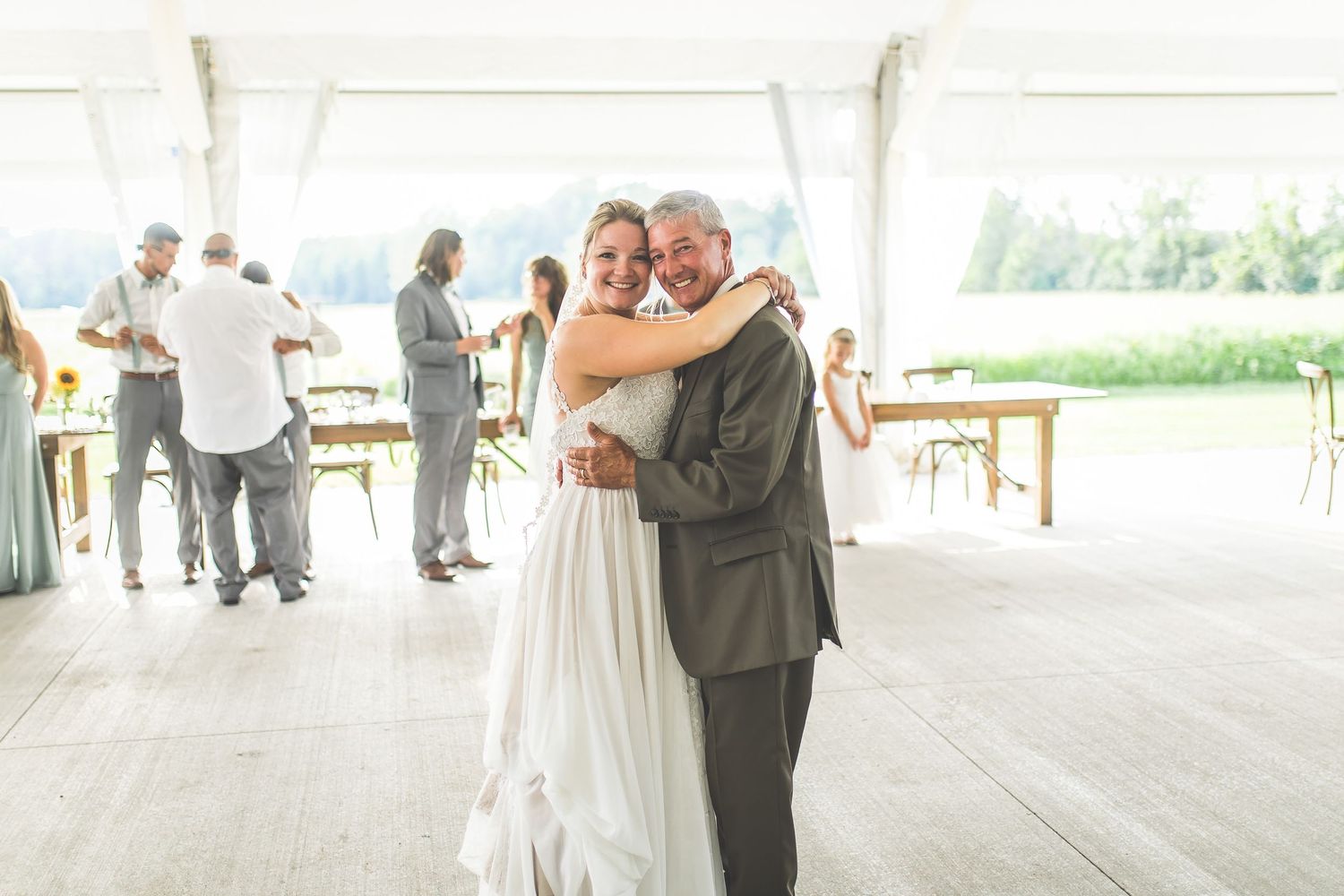A couple shares their first dance under a white tent at an outdoor wedding reception.