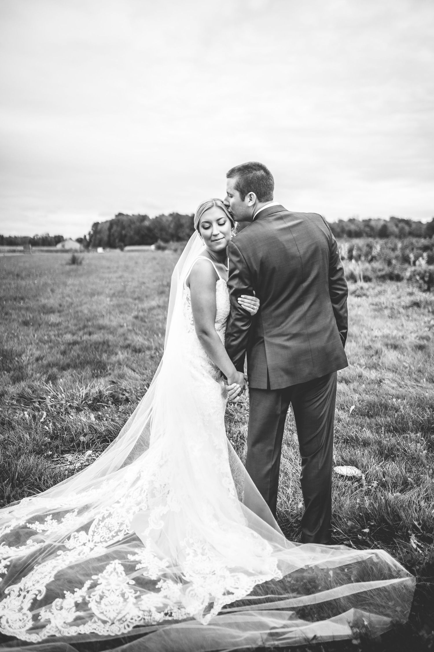 Beautiful wedding dress train spreads across grass as couple shares intimate moments outdoors.