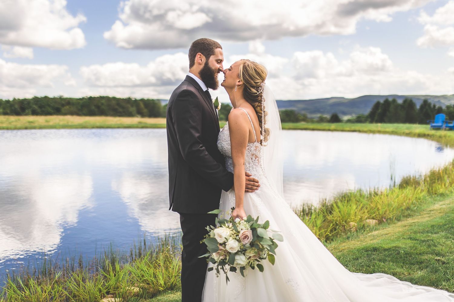 Romantic wedding photo by a lake with mountains and dramatic clouds in background.