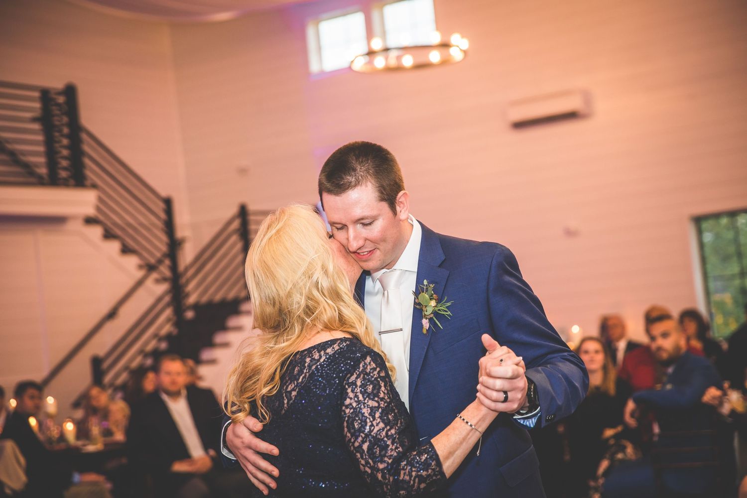 A couple shares an intimate dance moment at a wedding reception while guests look on from their seats.