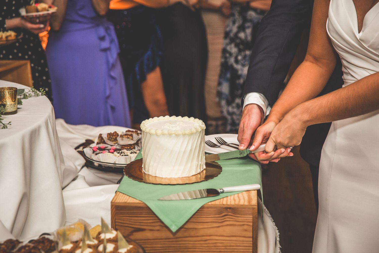 Wedding cake display with white frosting on wooden table at reception.