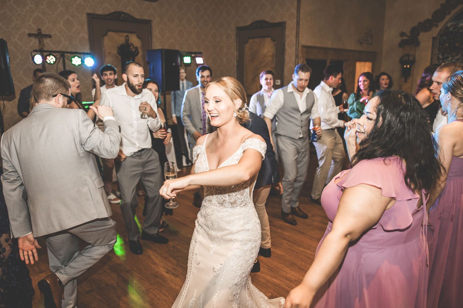 Wedding celebration with guests dancing in formal attire on a wooden dance floor.
