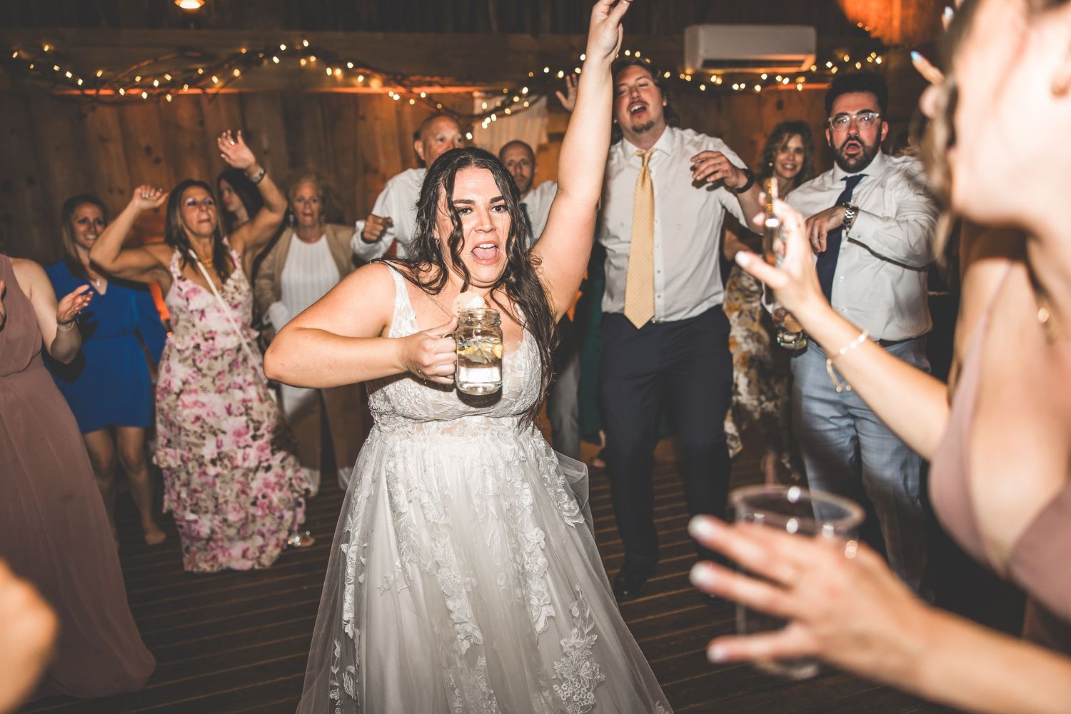 Wedding guests dancing and celebrating on a dimly lit dance floor at an evening reception.