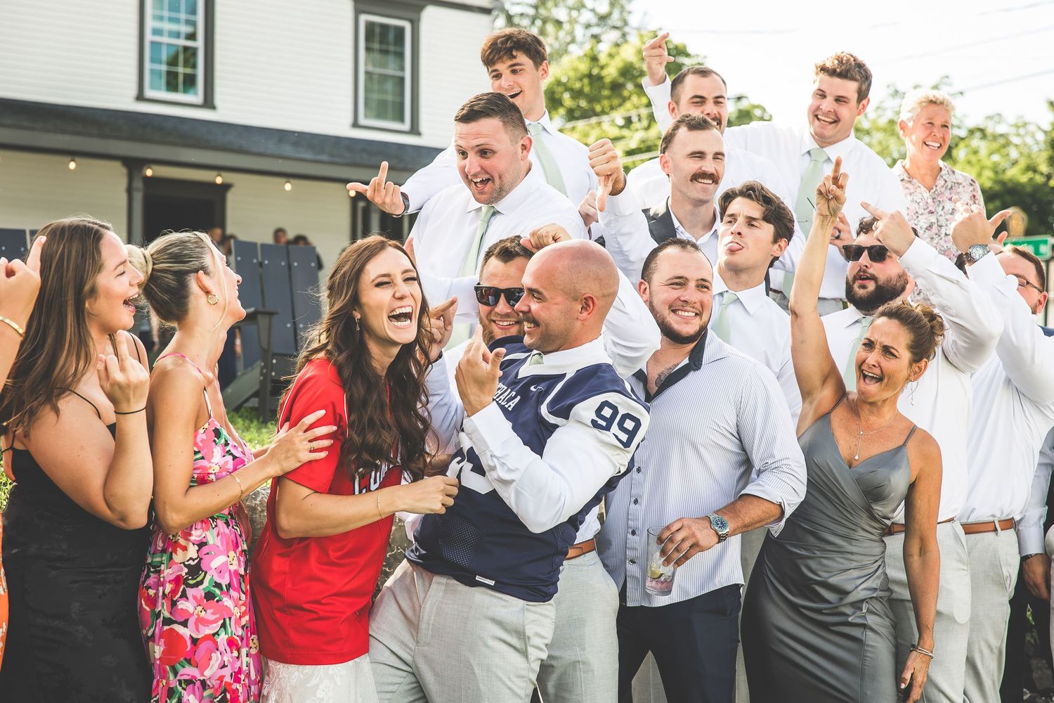Wedding party celebrating and dancing together outdoors during a summer reception.
