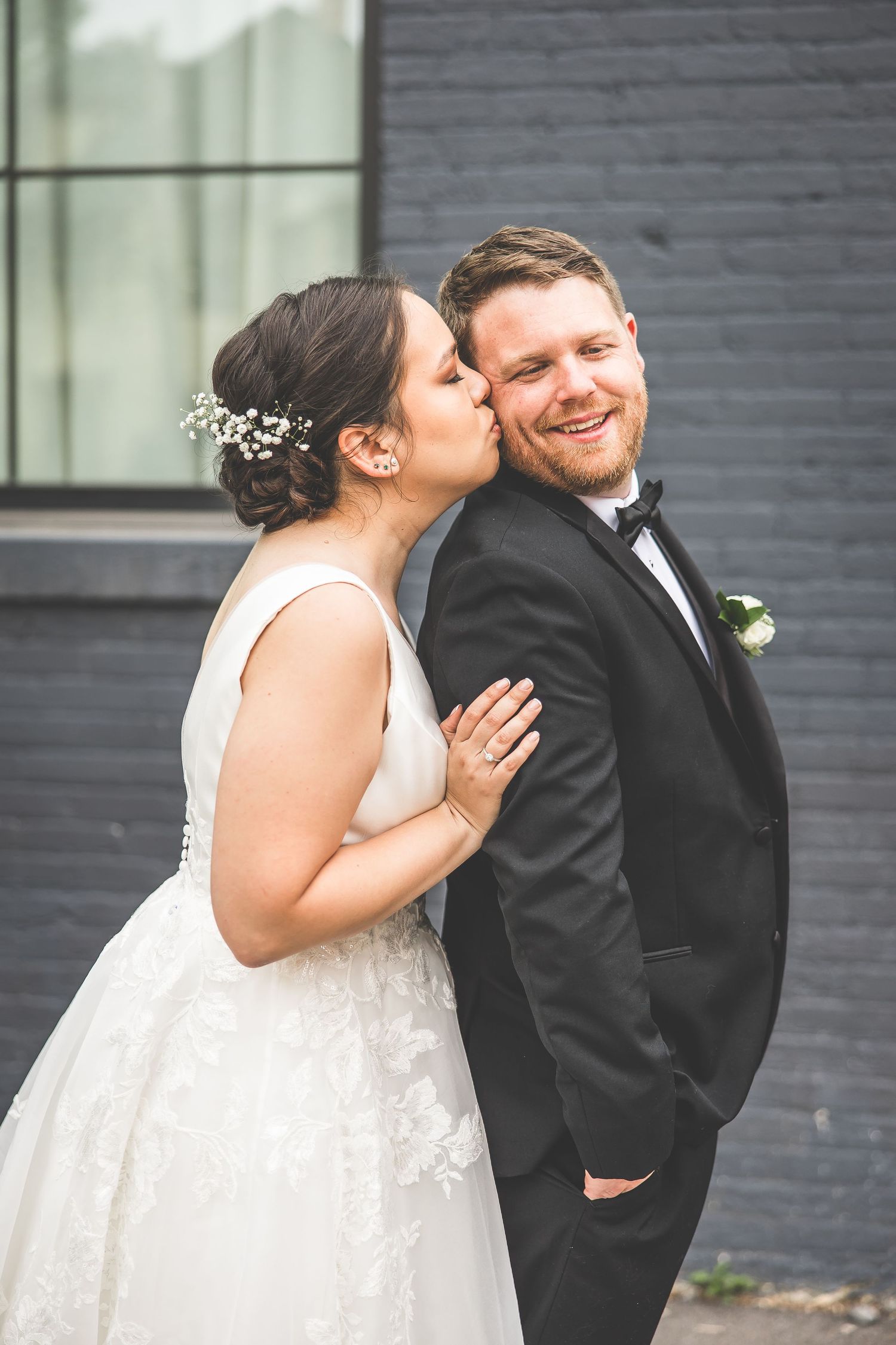 Candid wedding moment shared against a modern grey brick exterior.