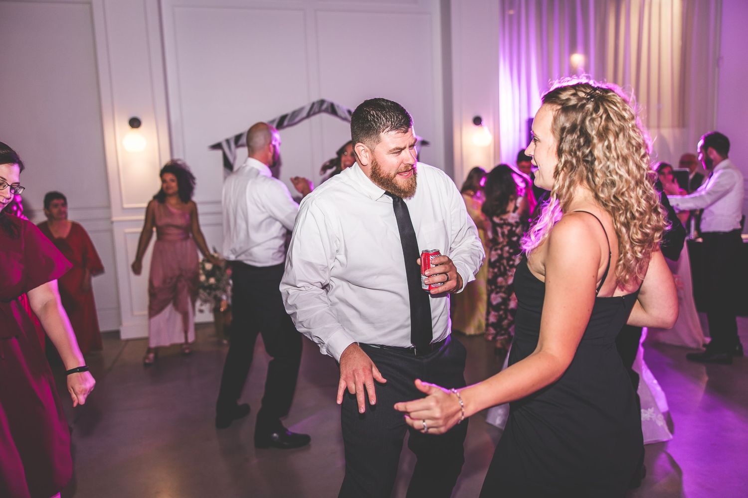 Reception venue illuminated with purple lighting as guests dance and celebrate.
