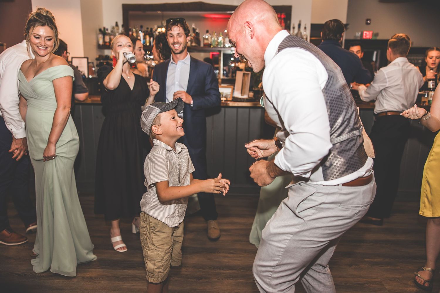 Wedding guests dancing and mingling on wooden dance floor during reception.