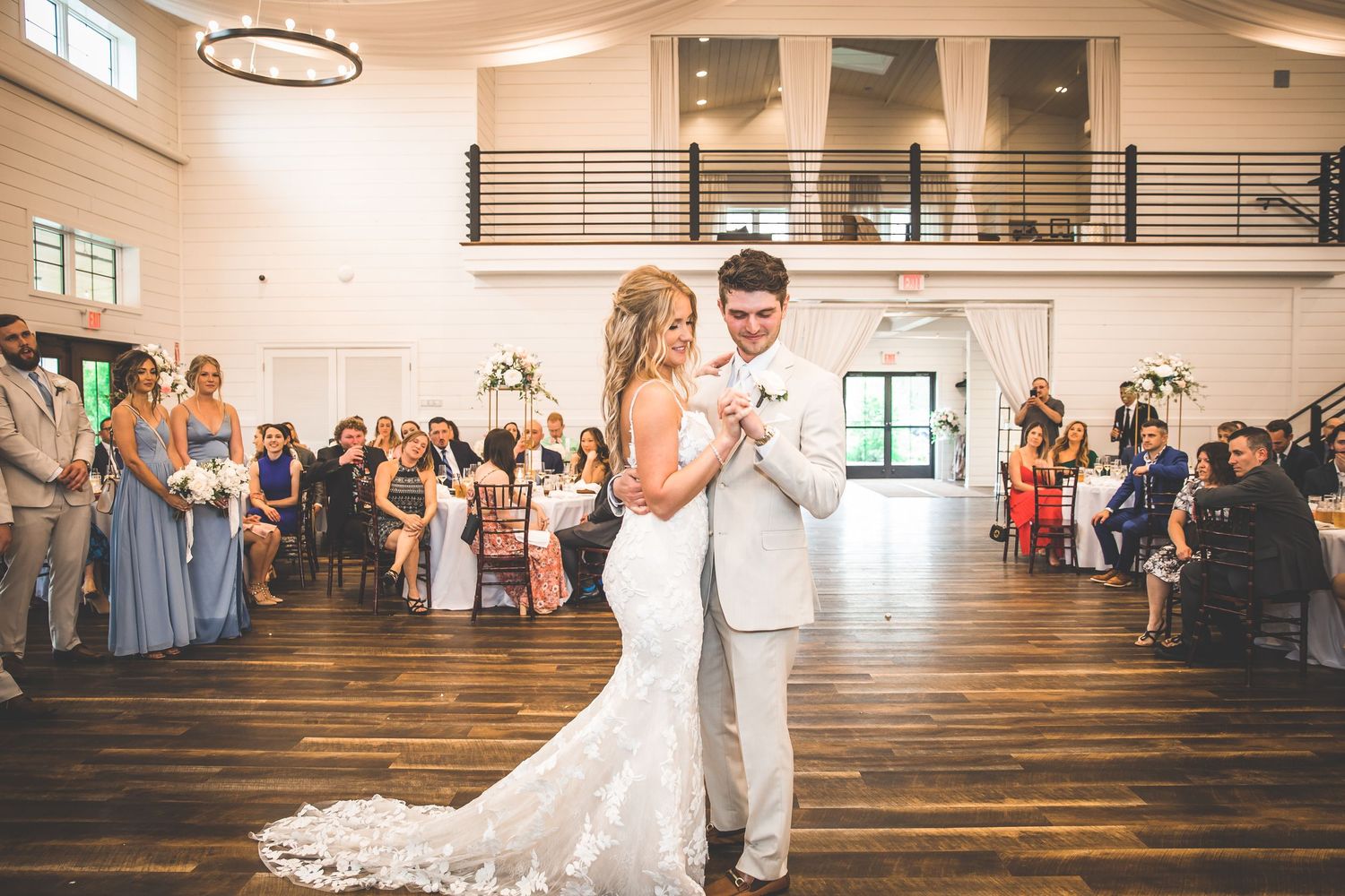Couple shares their first dance at an elegant wedding reception in a bright venue with guests watching.