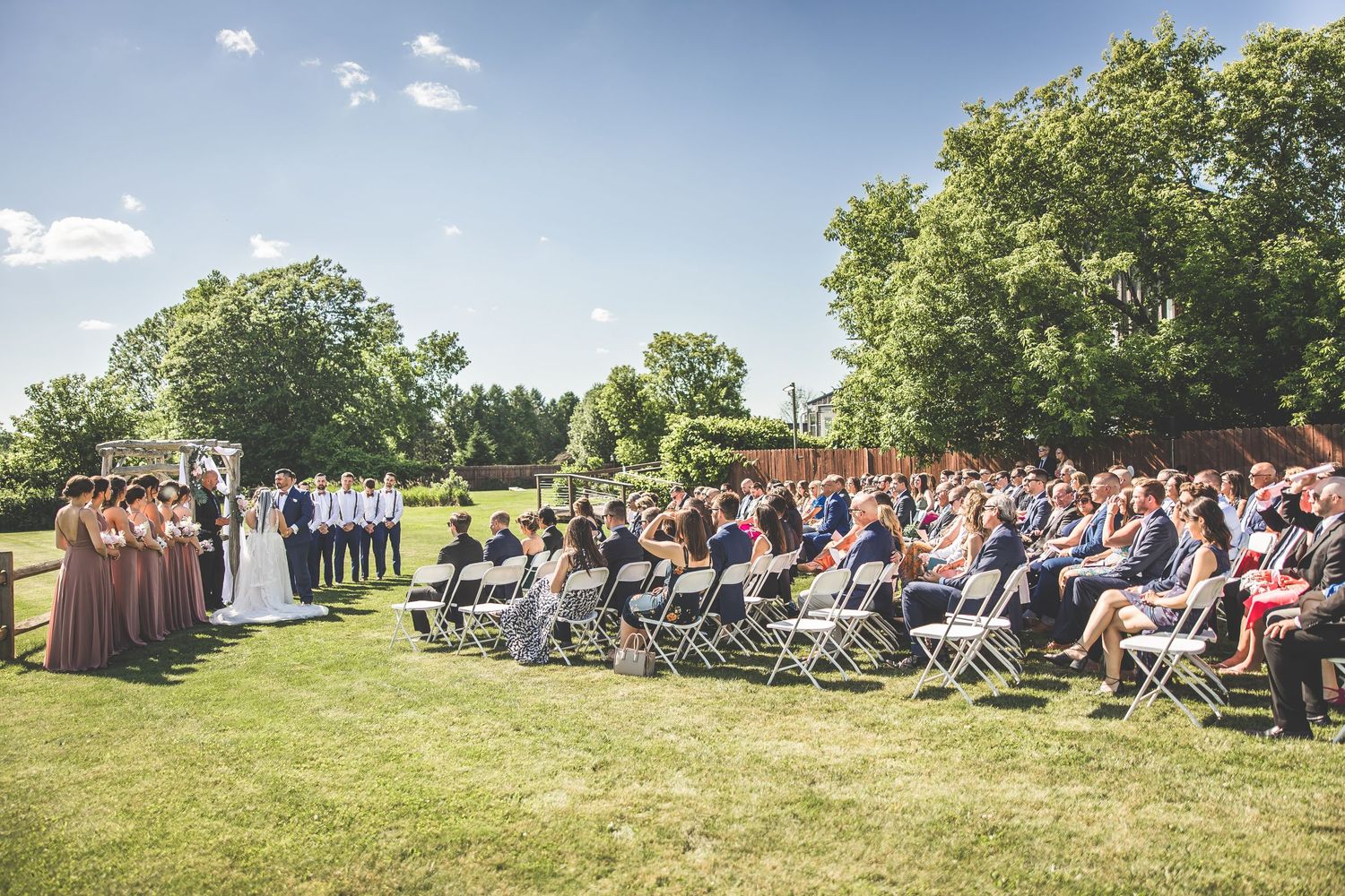 Wide angle view of wedding guests seated in rows for an outdoor ceremony on a hillside.
