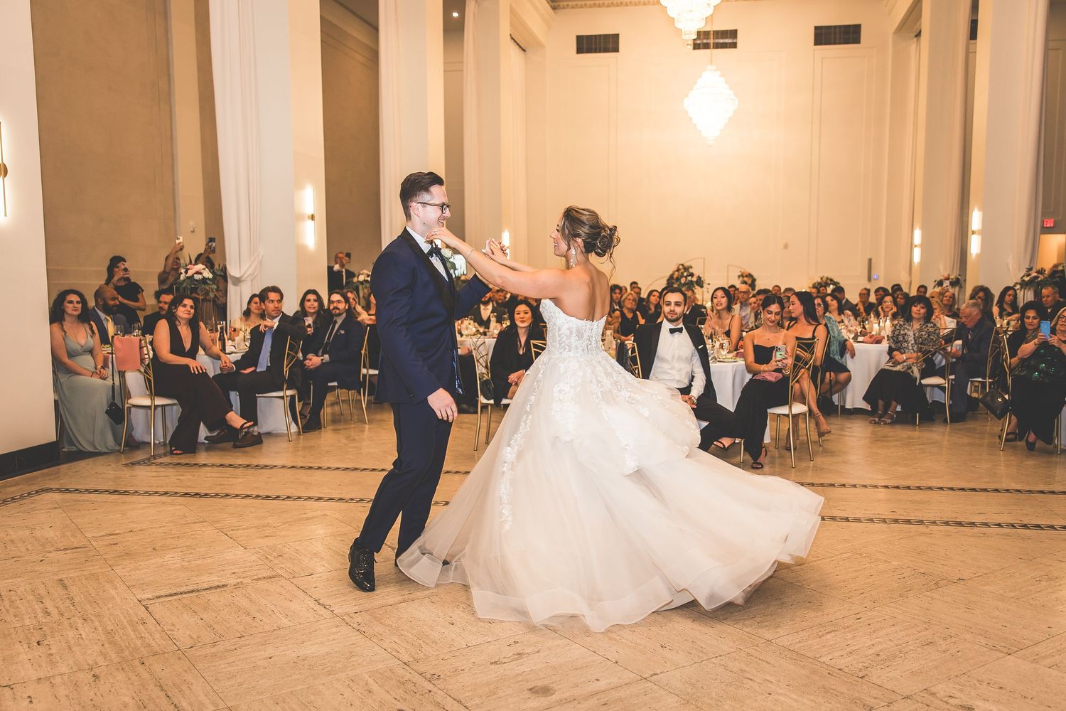 Wedding dance performance captured in warm lighting with audience seated along walls.